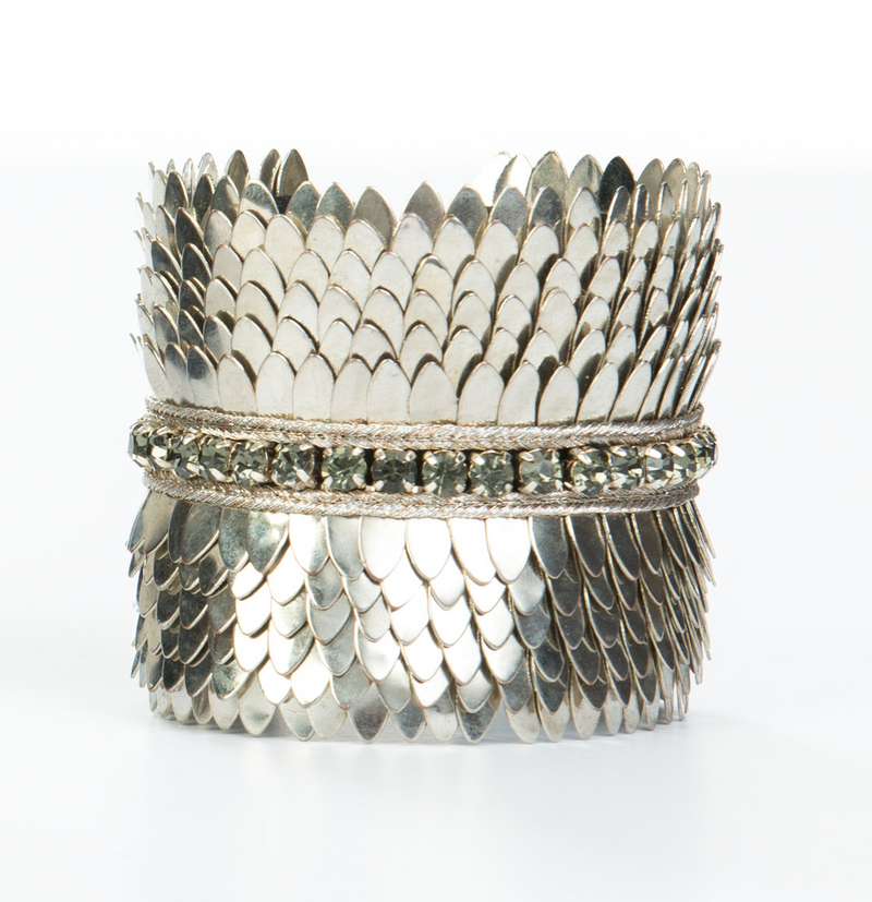 Wide gold plated cuff with feather cuts outs and a row of crystals in the center. The cuff is lined with soft leather for comfort. It is a significant piece that could be worn casually or to a black tie event.  It is offered in 3 finishes.