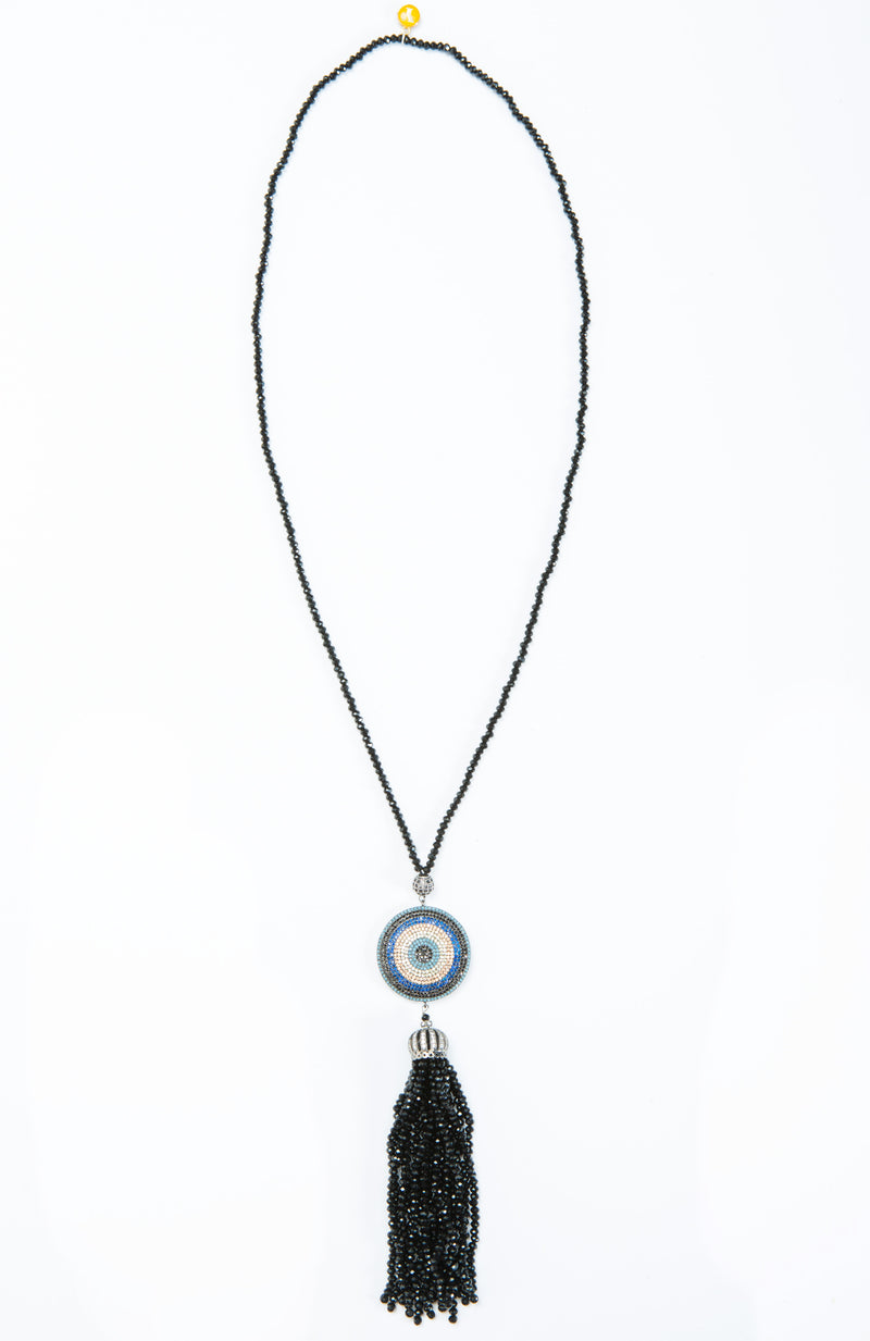 Classic evil eye dome tassel necklace with crystal and stone details. This necklace is worn long and is offered in shades of blue and black.