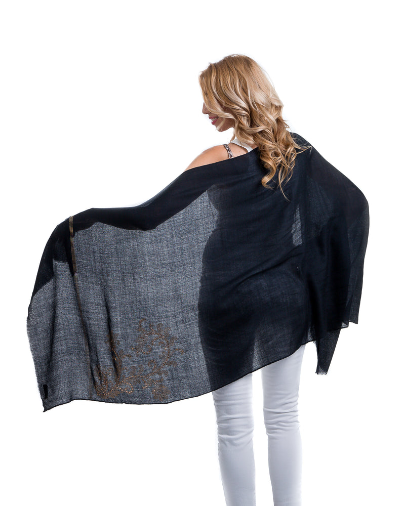 The image showcases the Yatra Halcyon Shawl that is offered in black and white. The cashmere shawl is decorated with large floral motifs at the two ends of the shawl with Swaravoski crystals in varied shapes and sizes. 