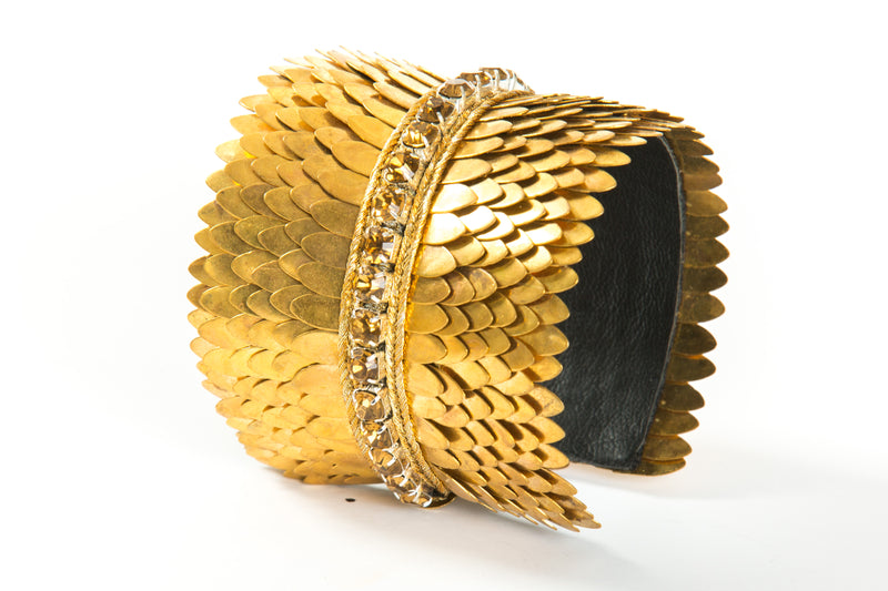 Wide gold plated cuff with feather cuts outs and a row of crystals in the center. The cuff is lined with soft leather for comfort. It is a significant piece that could be worn casually or to a black tie event.  It is offered in 3 finishes.