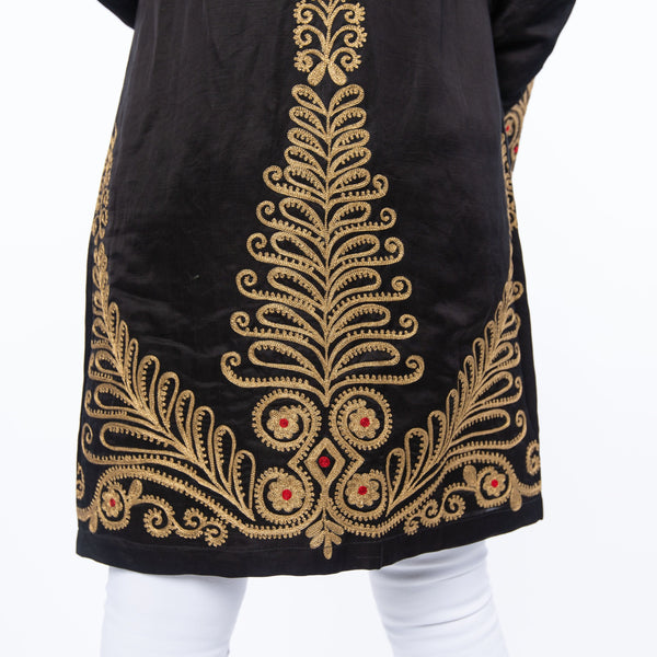 The image shows the Gwalior jacket. This is a highly embellished satin jacket that can be worn as a duster. The us extensive gold embroidery with red highlights on the back and sleeves of the of the jacket 