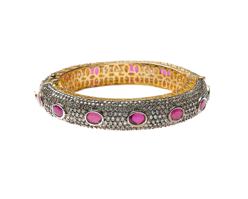 Hand-crafted bracelet with hinge in the center is easy to wear. The cuff is covered in clear Swarovski crystals. Semi precious red oval stones are spaced in intervals along the cuff.There is delicate filigree detail on the inside of the bracelet. The bracelet is 18k gold plated. 