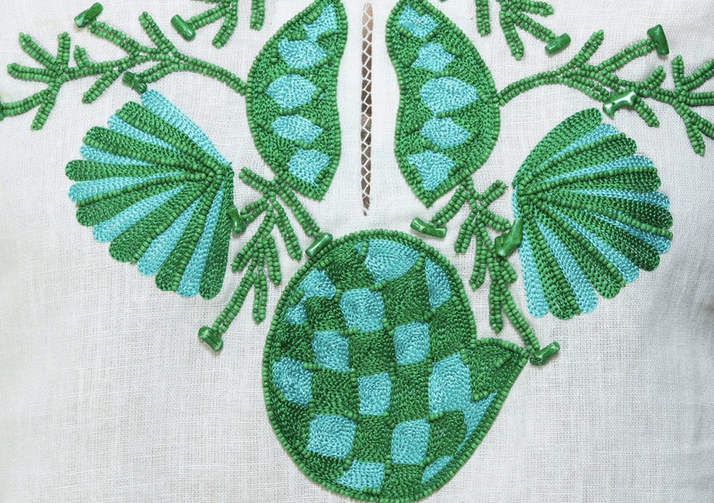 White linen tunic with substantial hand embroidery with faux coral detail. The embroidery is in either green, red or blue. Embroidery detail in around the neck, sleeves and at the bottom of the tunic. 