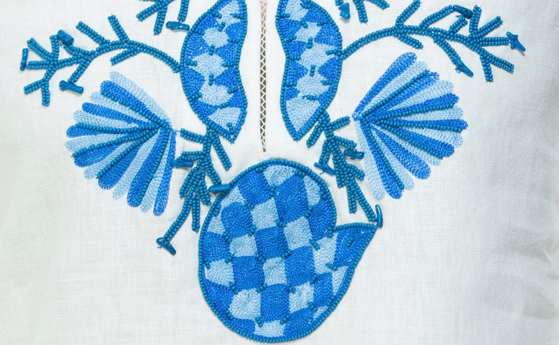 White linen tunic with substantial hand embroidery with faux coral detail. The embroidery is in either green, red or blue. Embroidery detail in around the neck, sleeves and at the bottom of the tunic. 