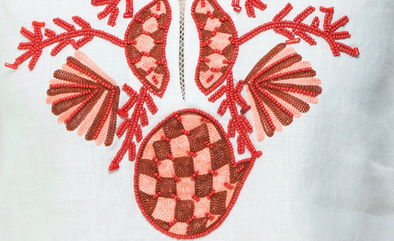 White linen tunic with substantial hand embroidery with faux coral detail. The embroidery is in either green, red or blue. Embroidery detail in around the neck, sleeves and at the bottom of the tunic. 