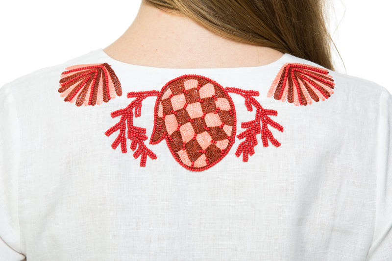White linen tunic with substantial hand embroidery with faux coral detail. The embroidery is in either green, red or blue. Embroidery detail in around the neck, sleeves and at the bottom of the tunic. 