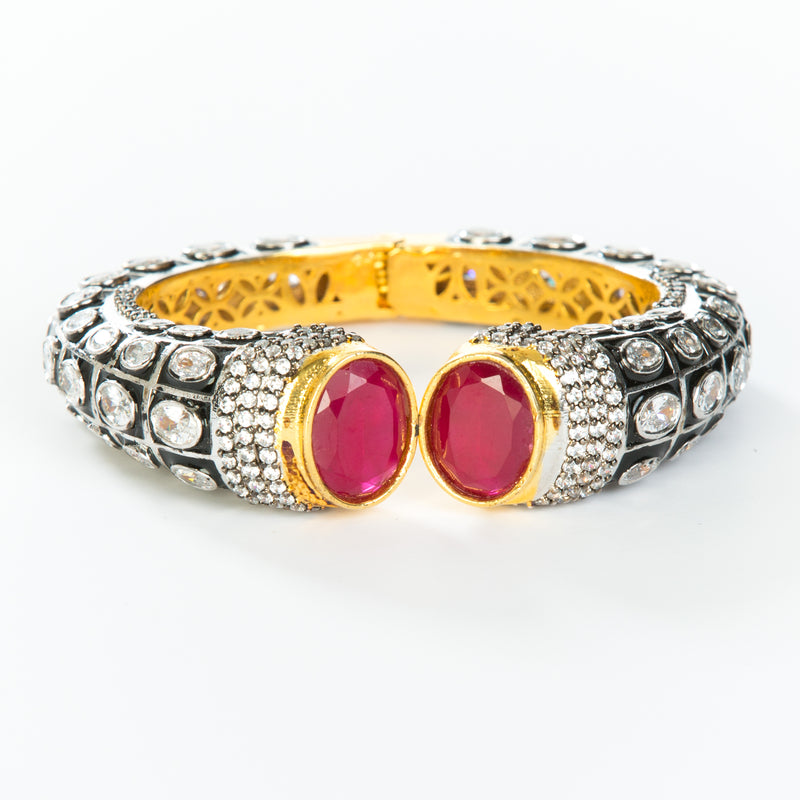 The images shows the Yatra.shop signature cuff. It is an easy to wear cuff with a hinge in the center. This cuff fits most wrists. It is embellished with enamel, Swarovski crystals of varying shapes and sizes and there are two round red semi precious stones at the opening. 